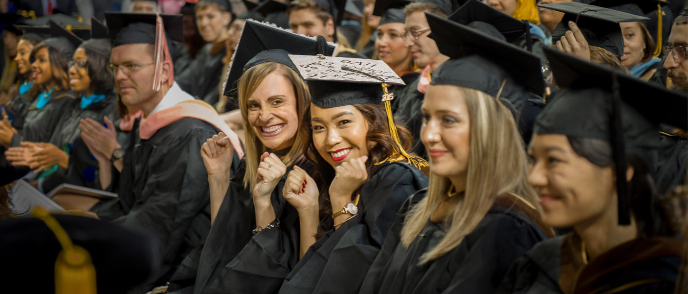 Graduates in caps and gowns smile at the camera